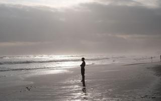 person standing on beach looking out at ocean, black and white photo