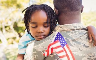 Army veteran holding young child who is holding a US flag at a memorial service