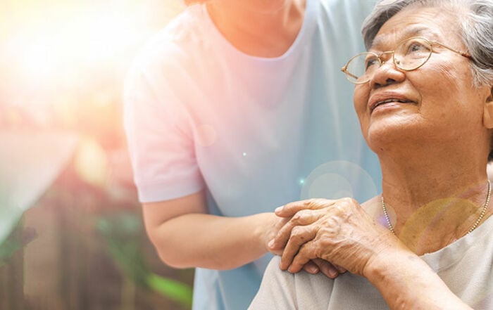 woman with hand on shoulder of elderly parent in hospice care, outdoors in California